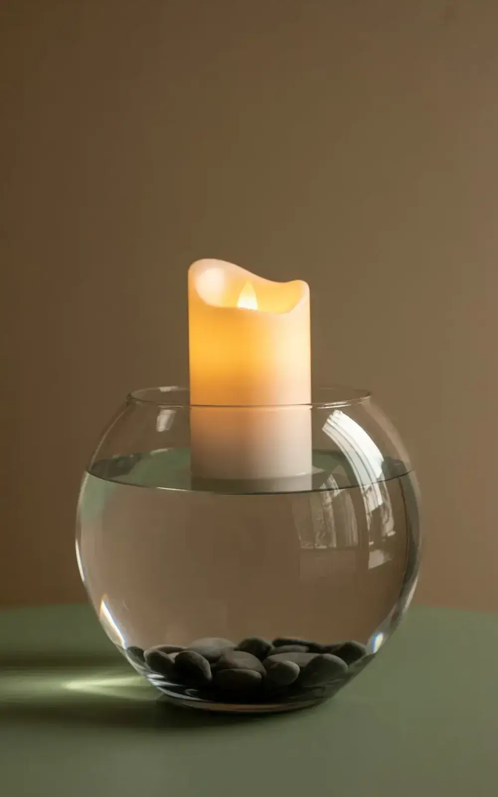A lit candle in a glass bowl filled with smooth grey pebbles.