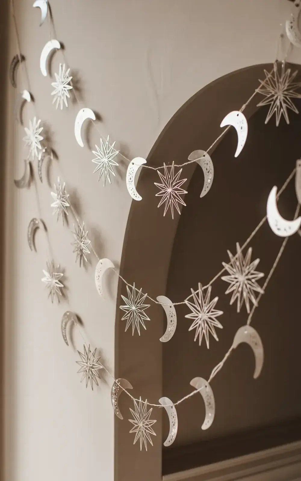 White paper moon and star decorations hanging from a curved wall Чаrund a window.