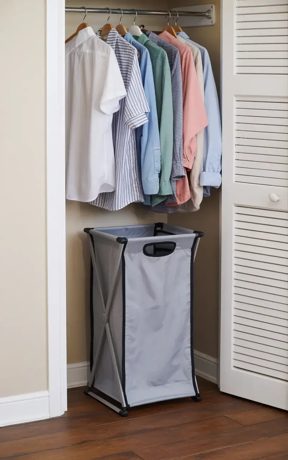 Clothes hanging in a closet with a laundry basket on the floor.
