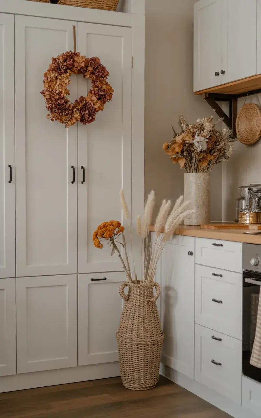 Fall-themed dried flowers in woven vases and a wreath on white kitchen cabinets