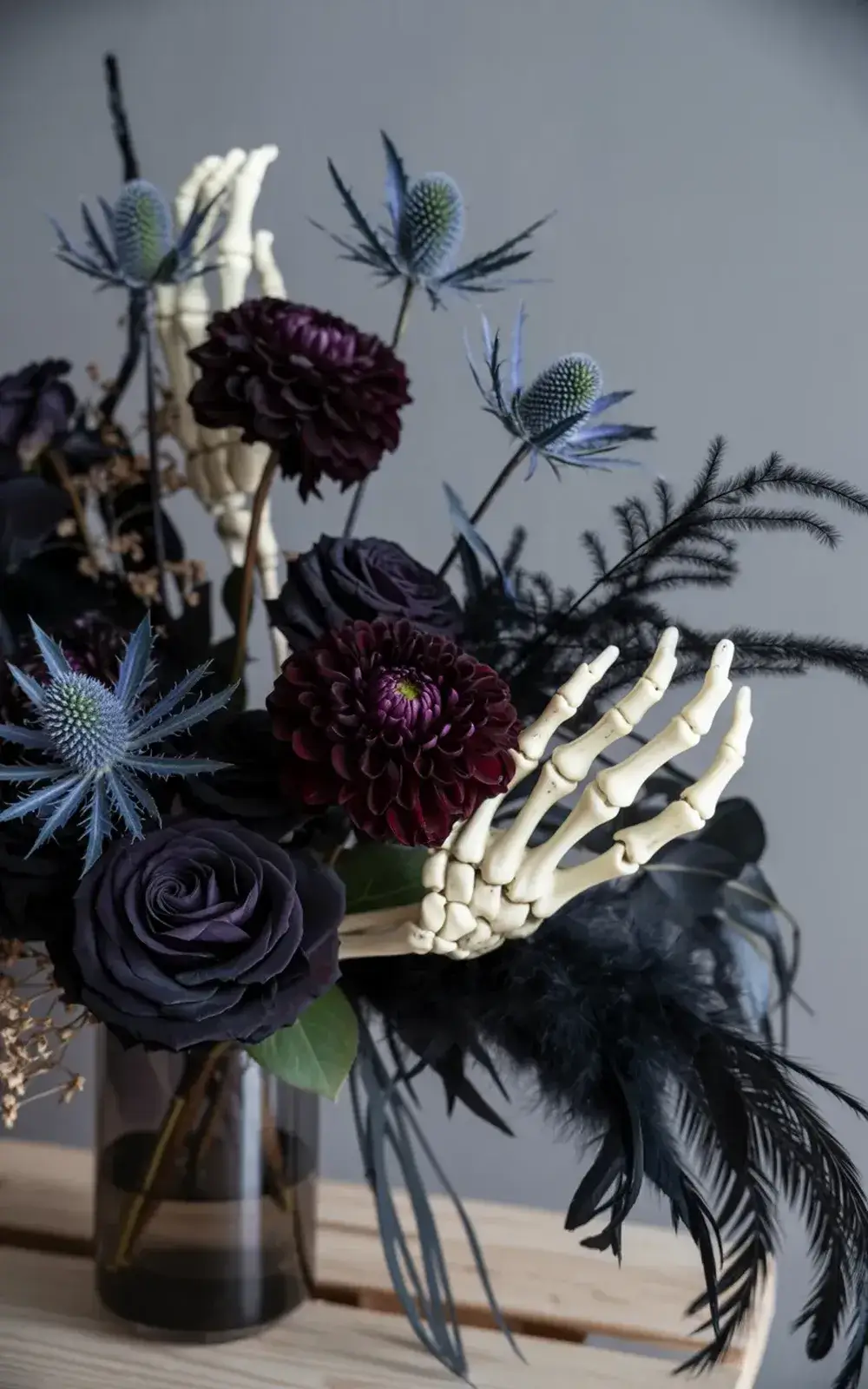 Flower arrangement featuring dark purple flowers and thorns, feathers, and skeleton hands.
