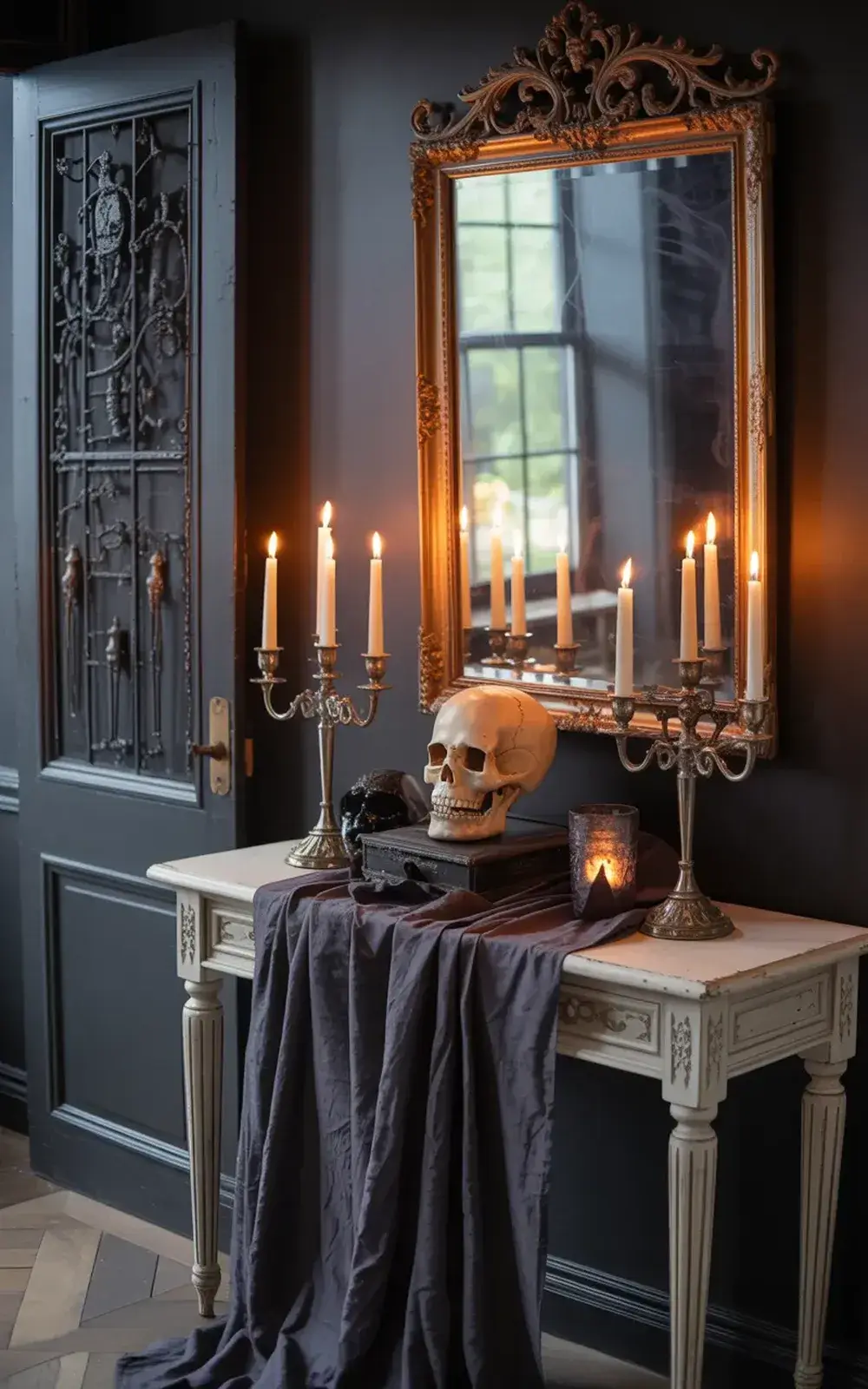 Two ornate tables draped with dark fabric hold lit candle holders and a skull in front of an ornate mirror and wrought iron door.