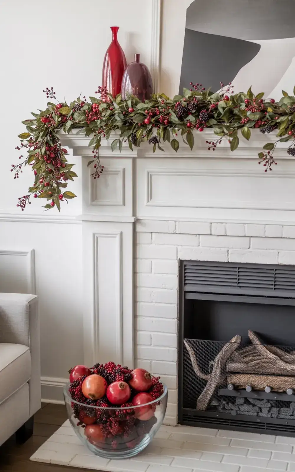 A decorated fireplace mantle with greenery, berries, vases, and a bowl of fruit.