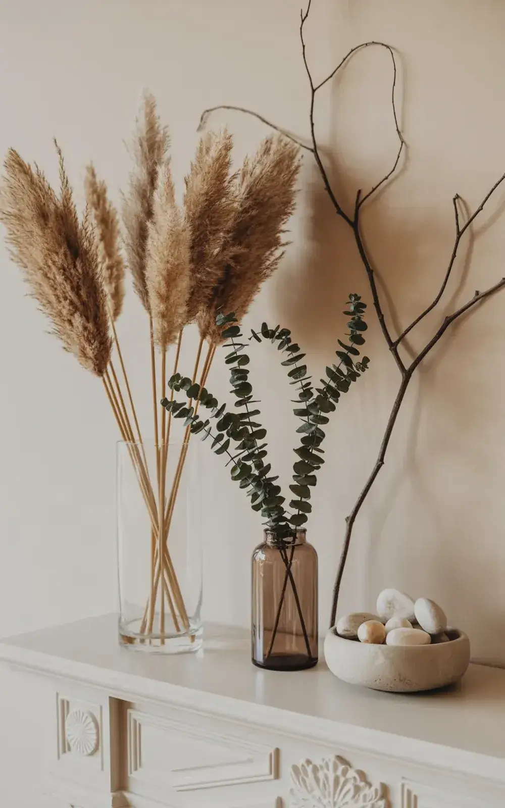 Decorative shelves with pampas grass, eucalyptus, branches in two vases, and a bowl of smooth stones.