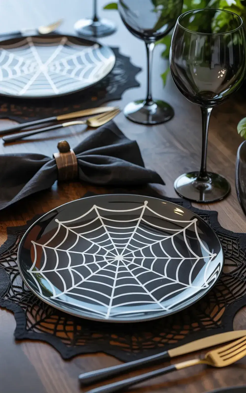 Halloween-themed place setting with spider web plate, wine glasses, and black napkins.